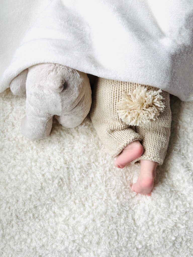 Tiny baby feet and a soft toy elephant under a blanket
