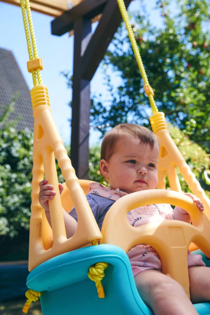 Baby sitzt in einer bunten Kinderschaukel im Garten