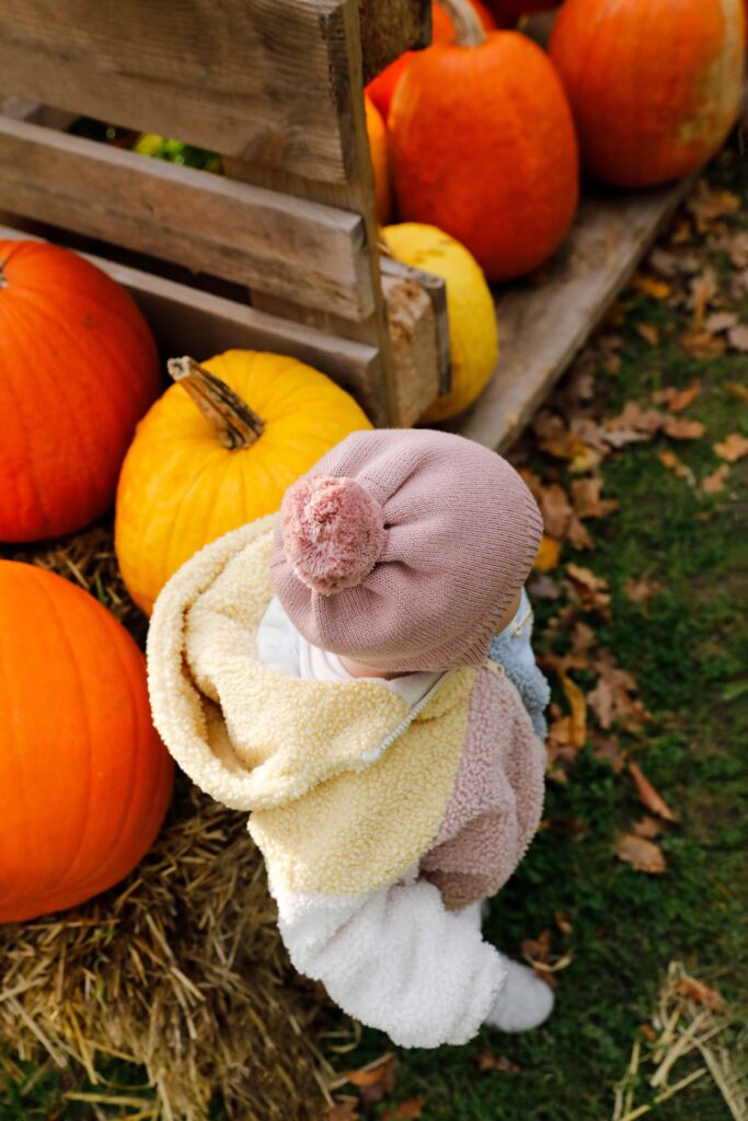 Baby sitzt zwischen Kürbissen und Stroh bei einem Herbst-Fotoshooting