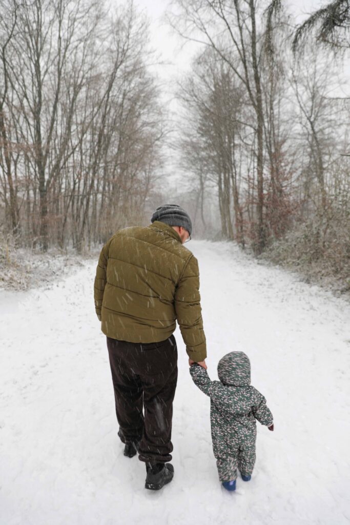 Vater und Kind gehen Hand in Hand durch eine verschneite Landschaft