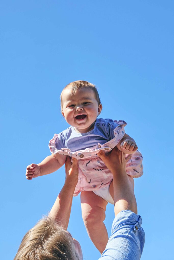 Baby wird von einem Erwachsenen lachend in die Luft gehoben