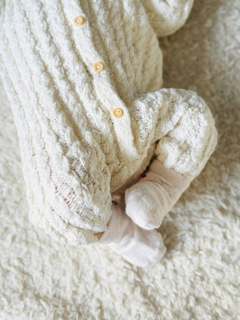 Detail of a baby wrapped in a knitted blanket with a soft toy