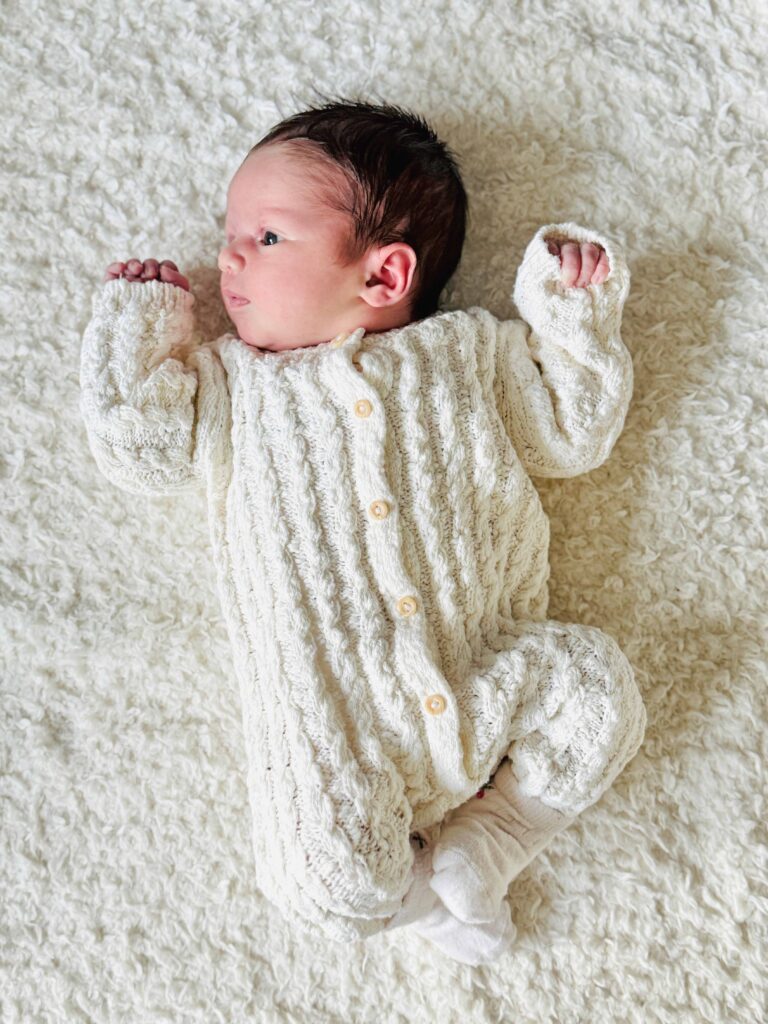 Four-month-old baby in a light knitted outfit on a blanket