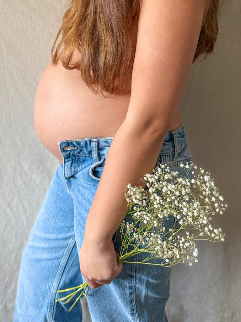 Pregnant woman with a baby bump holding a bouquet of white flowers