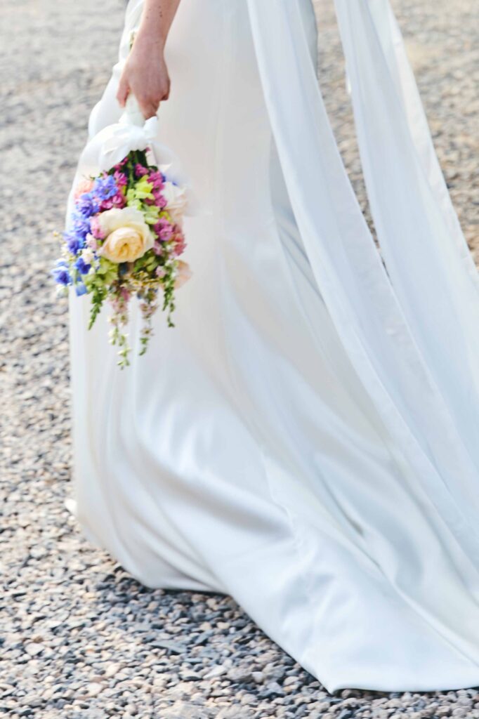Bunter Brautstrauß neben dem fließenden Brautkleid