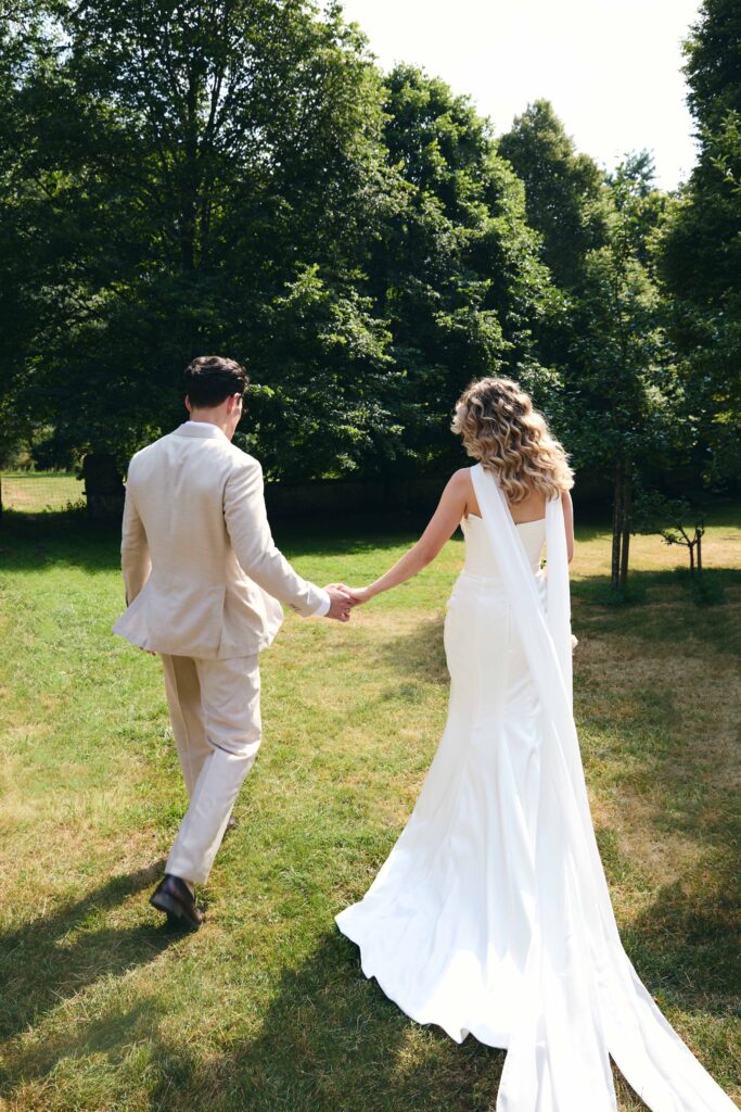 Bride and groom walking hand in hand across a meadow